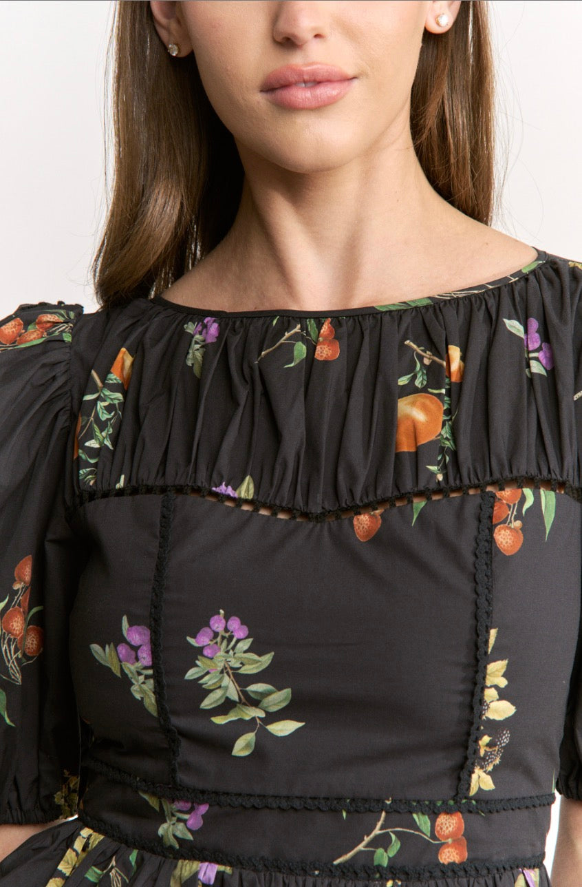 Close-up of a model wearing a black puff-sleeve top with a gathered ruffle neckline and an orange and purple floral print.