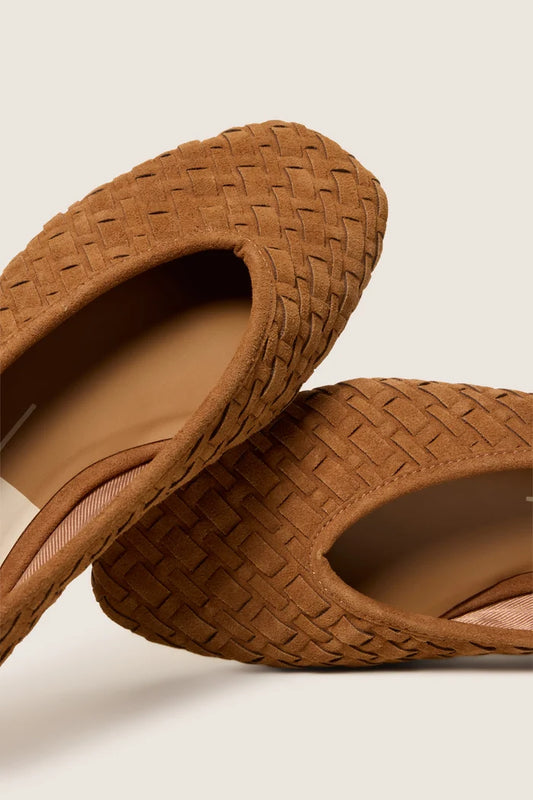 A close-up of a pair of women's woven mule slippers in a warm tan-brown suede-like material, displayed on a light beige background.