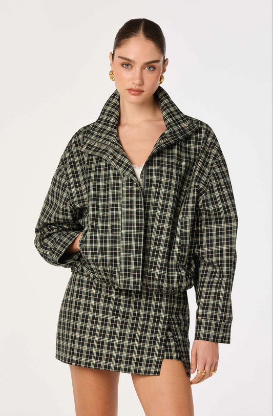 A model wearing a dark green and black plaid jacket and matching mini skirt set against a plain white studio background.