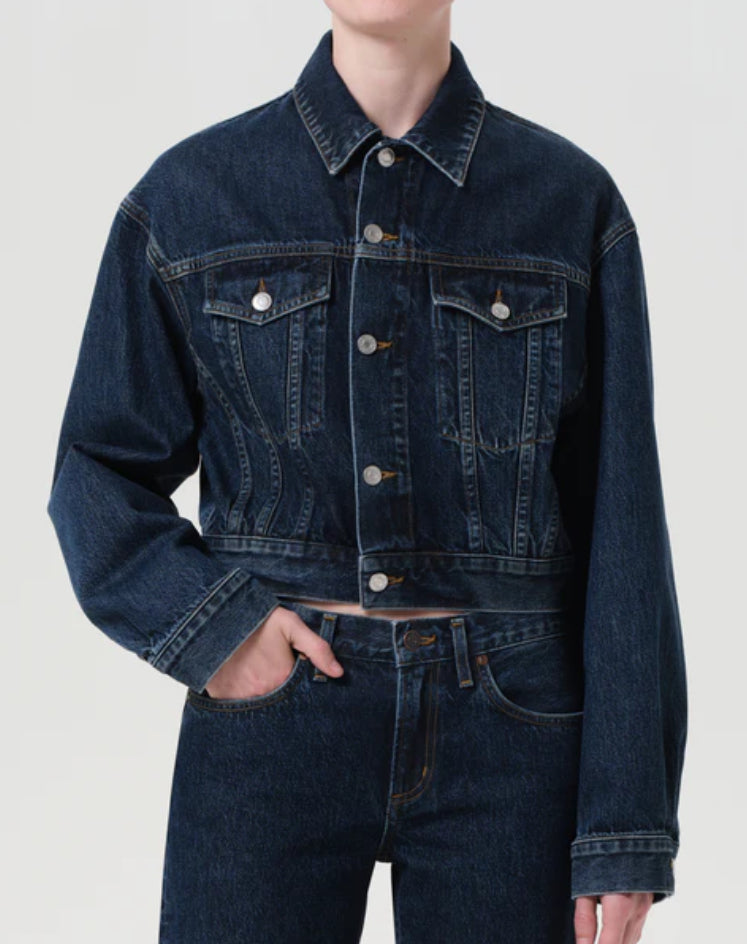 Person wearing a dark blue denim jacket and jeans on a light gray background