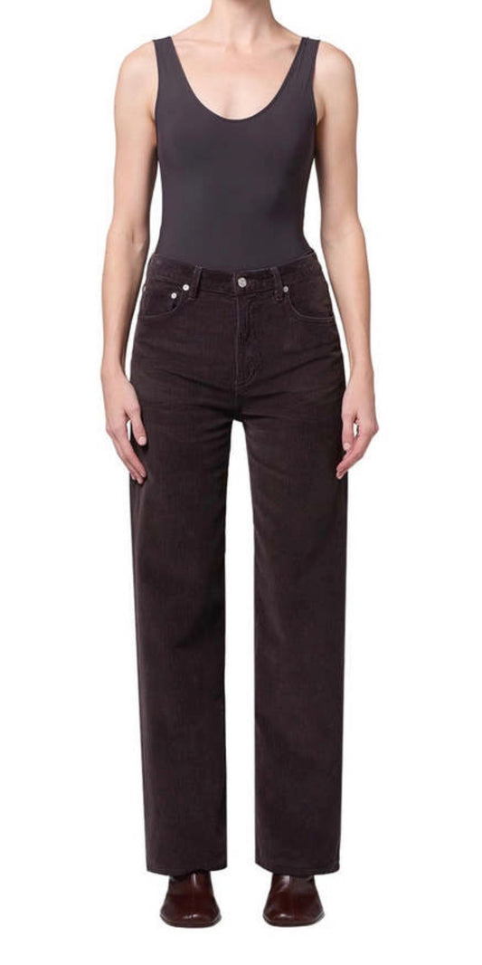A model wearing a dark charcoal gray sleeveless bodysuit and dark brown wide-leg corduroy pants, paired with dark brown leather shoes, against a plain white background.