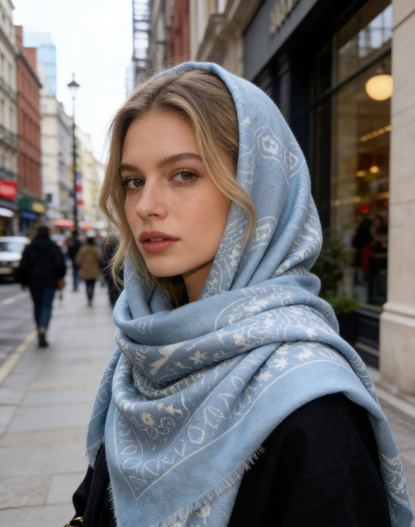 Woman wearing a light blue scarf with a pattern on a city street.
