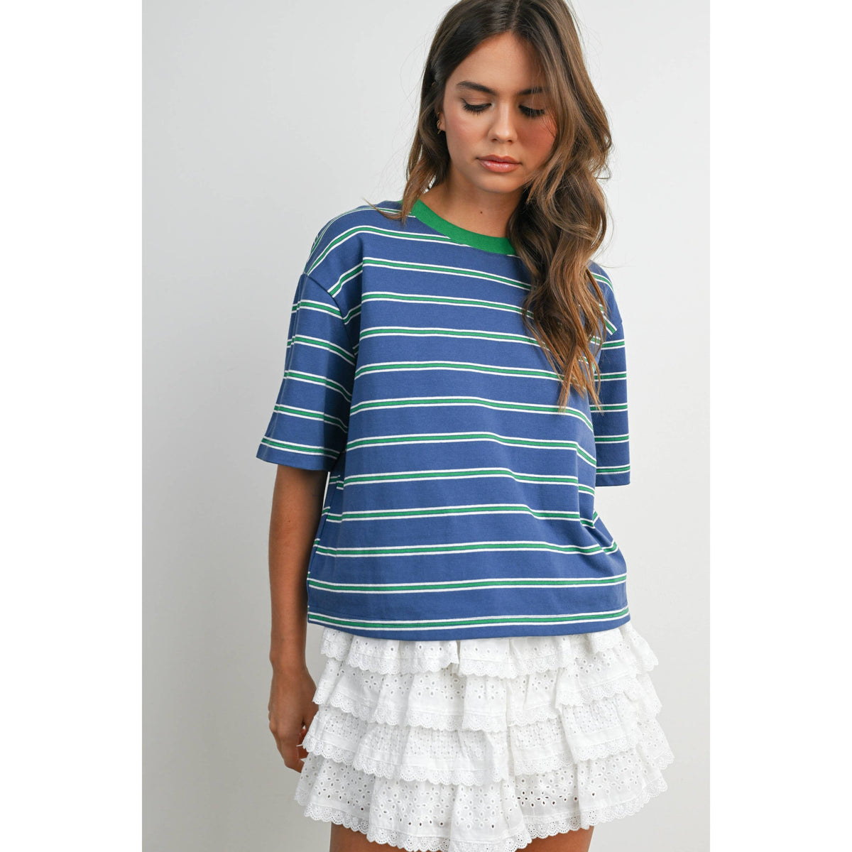 Woman wearing a blue and green striped shirt with a white ruffled skirt on a plain background