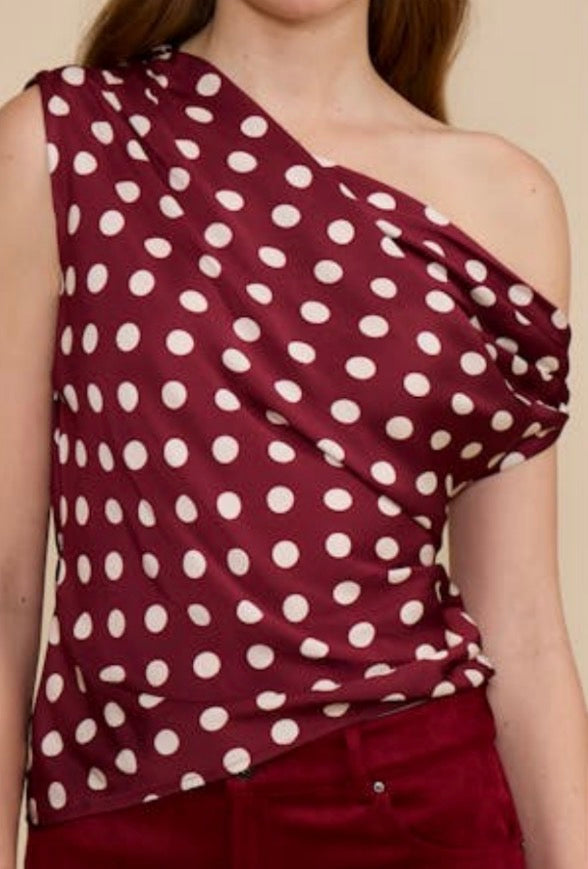 A close-up of a woman wearing a one-shoulder draped top in burgundy with white polka dots, paired with matching burgundy bottoms.