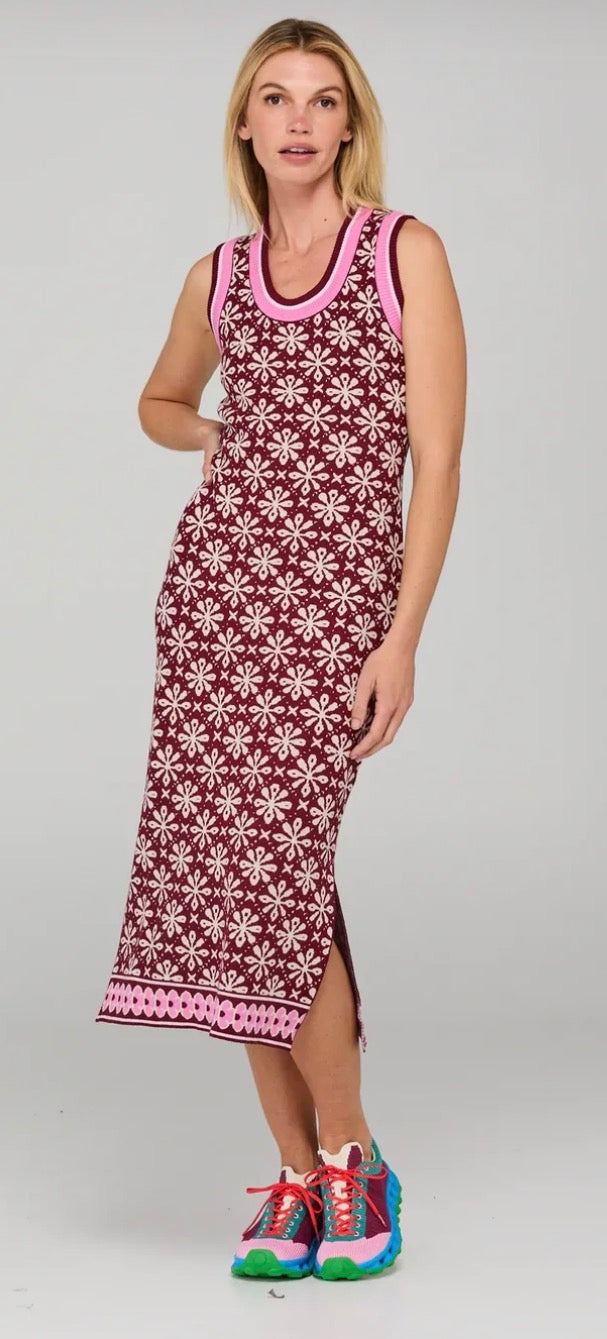 A woman modeling a sleeveless midi dress with a burgundy and white floral pattern and pink trim, paired with colorful sneakers, against a light gray studio background.
