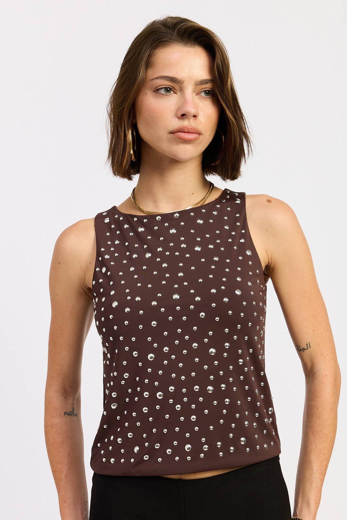 Woman wearing a brown sleeveless top with white pattern on a white background