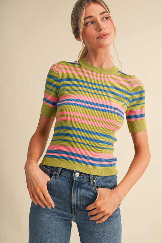 A woman wearing a short-sleeve ribbed knit top with horizontal stripes in olive green, pink, blue, and white, paired with blue jeans, against a solid beige background.