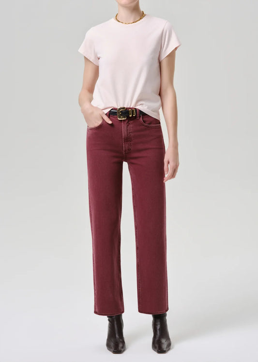 A model wearing a light pink short-sleeve t-shirt, dark red wide-leg jeans with a black belt, and black ankle boots, standing against a light gray studio background.