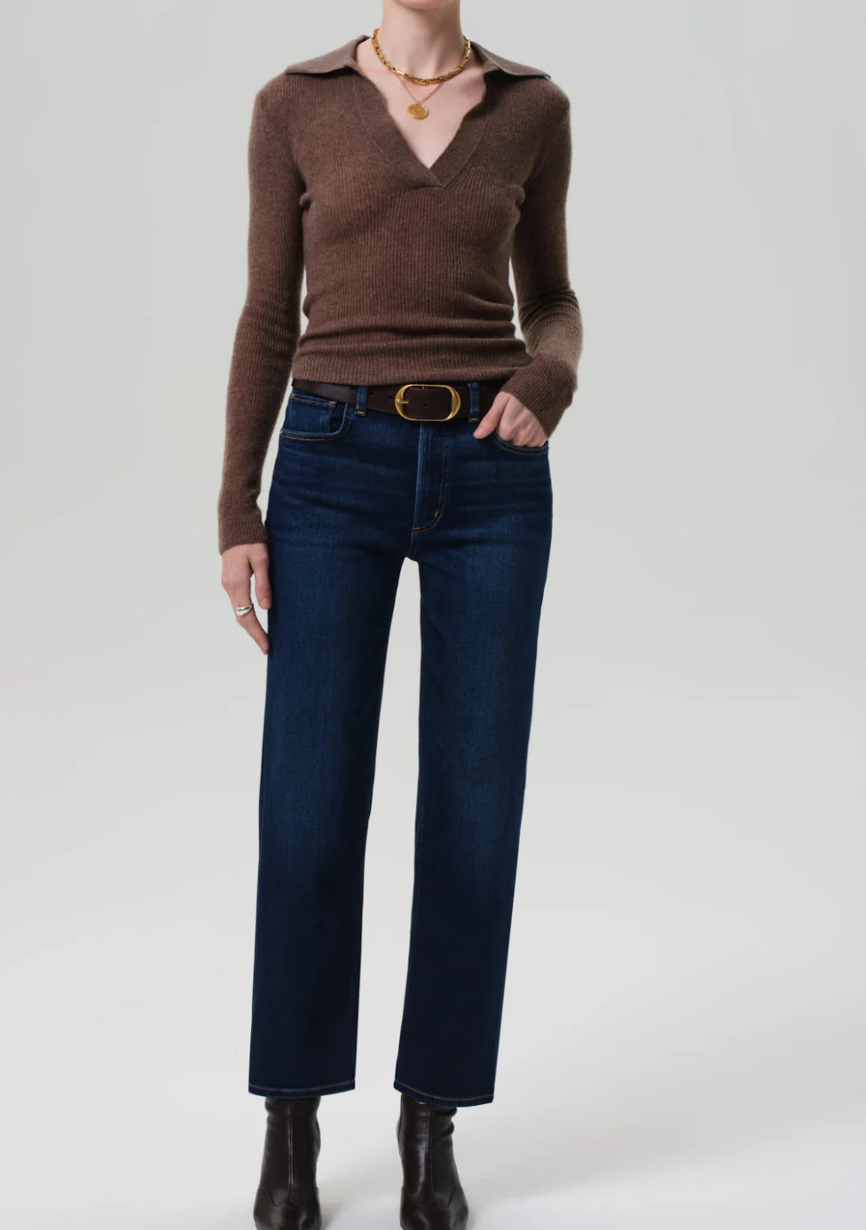 Person wearing a brown sweater, blue jeans, and black shoes on a white background