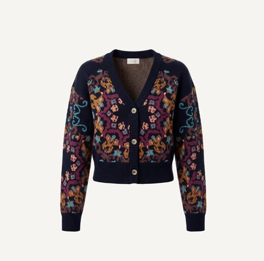A cropped cardigan sweater with a navy blue ribbed knit base and a vibrant multicolor floral and ornamental pattern across the body and sleeves, featuring three front buttons.