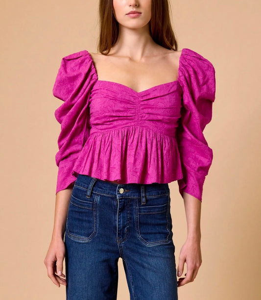 Woman wearing a pink top with puffed sleeves and blue jeans on a beige background