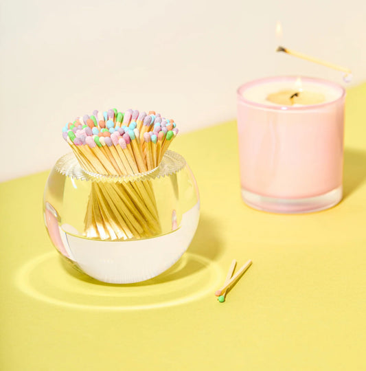 Glass container with colorful matches and a pink candle on a yellow surface