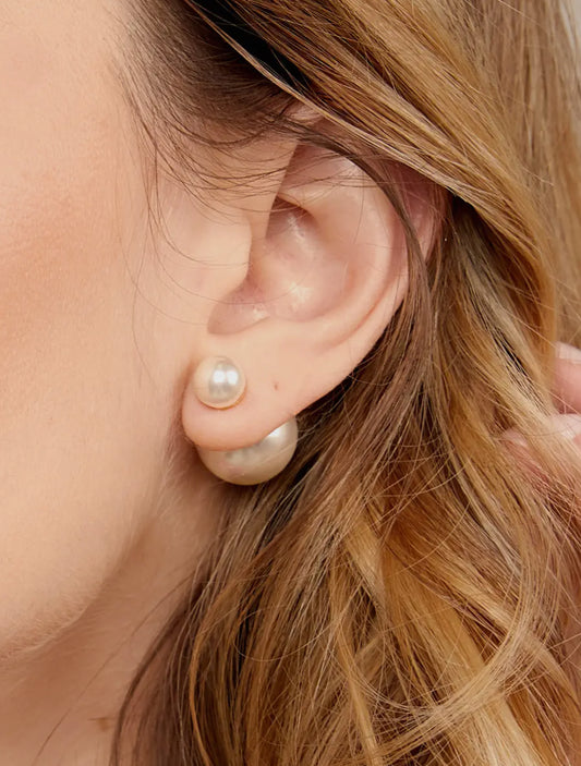 Close-up of an ear wearing two pearl earrings with a blurred background