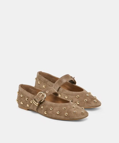 A pair of taupe suede Mary Jane flats decorated with gold-tone metal studs and buckles, shown against a light gray background.