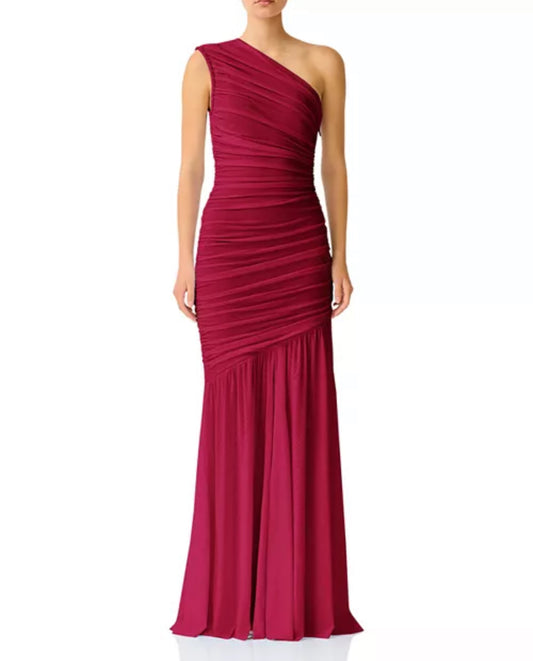 A woman modeling a floor-length, one-shoulder draped gown in a rich magenta-berry tone against a plain white studio background.