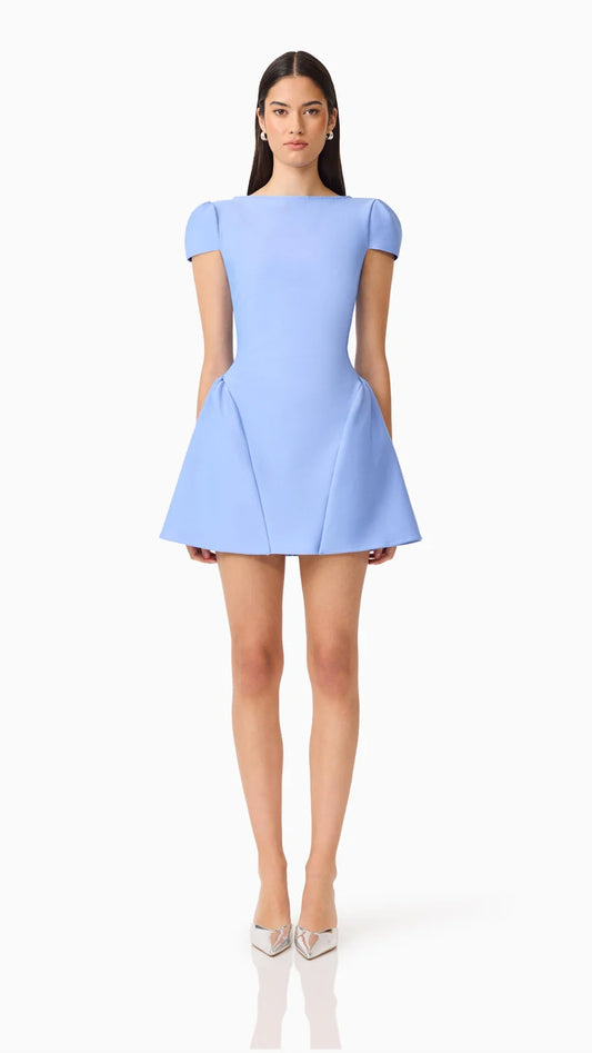 A woman modeling a light blue short puff-sleeve dress with a flared skirt, paired with metallic silver pointed-toe heels, against a plain white studio background.