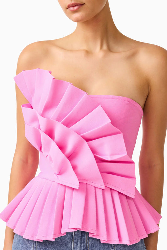 A bright pink strapless ruffled top with a structured peplum hem, shown on a model against a plain white background.