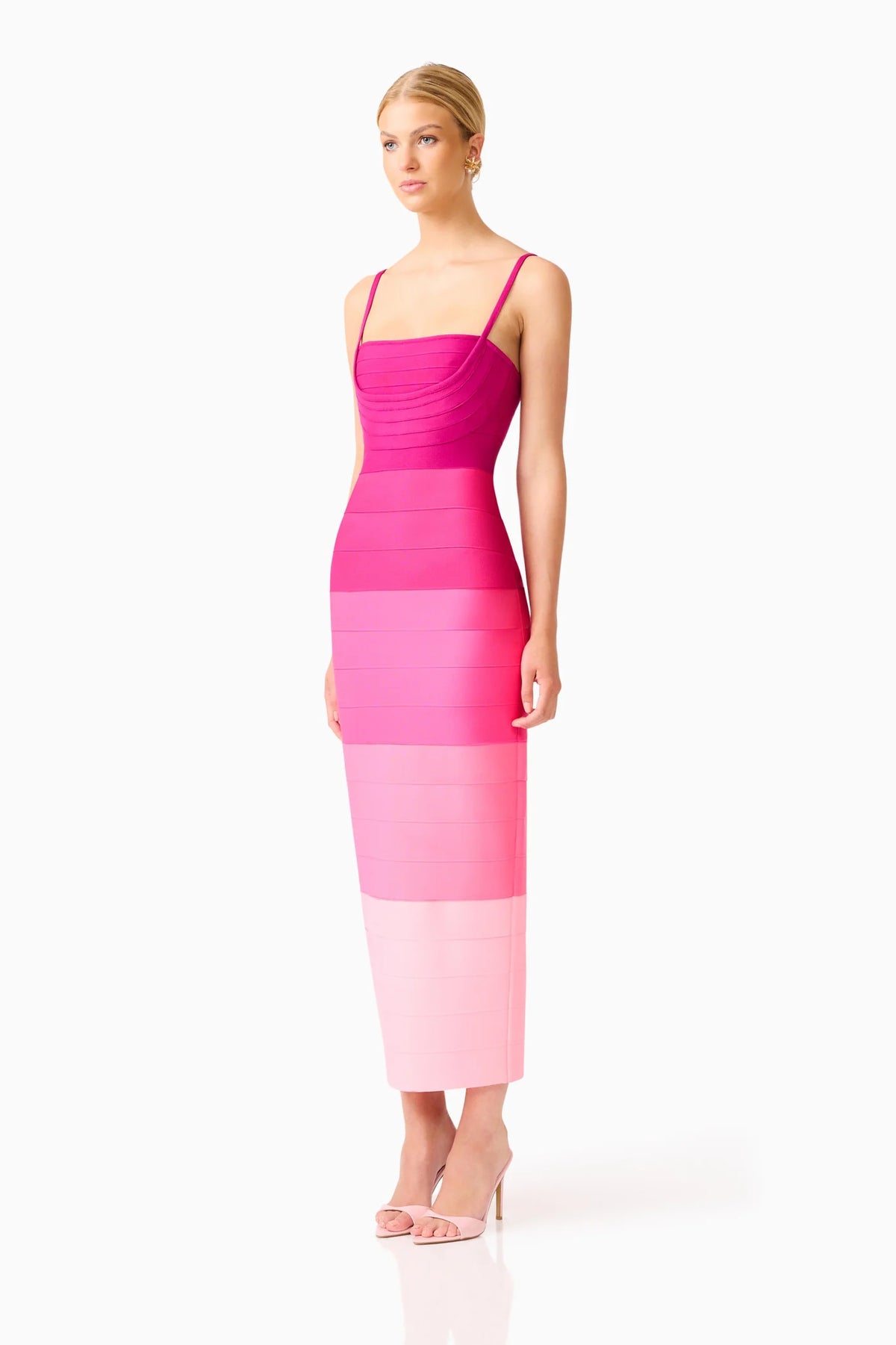A woman modeling a sleeveless midi dress with horizontal color-blocked bands in dark pink, bright pink, and pale pink, paired with clear high-heeled sandals, against a plain white studio background.