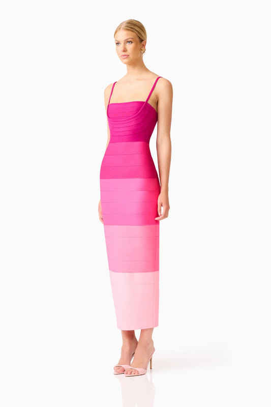 A woman modeling a sleeveless midi dress with horizontal color-blocked bands in dark pink, bright pink, and pale pink, paired with clear high-heeled sandals, against a plain white studio background.