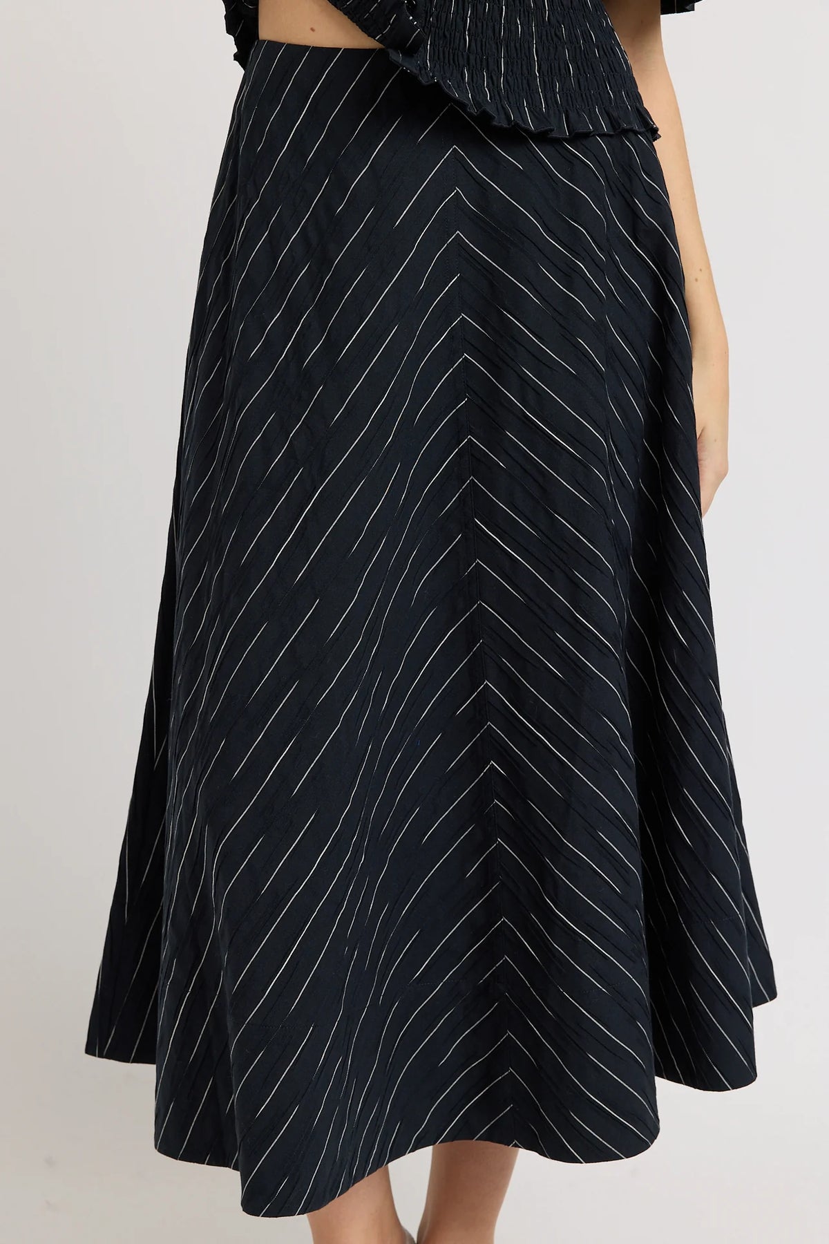 A black midi skirt with a white chevron stripe pattern, shown on a model against a light gray background.