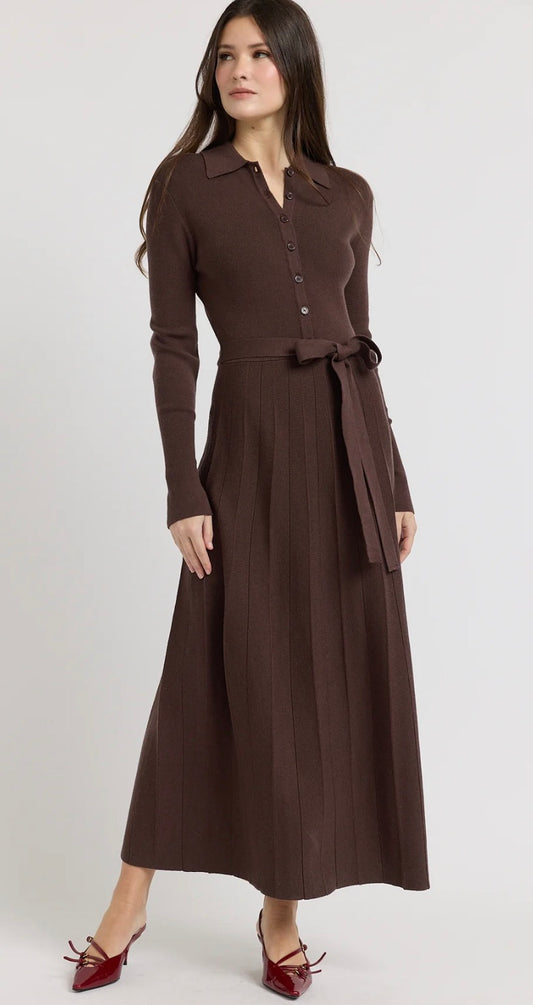 A woman modeling a long-sleeve brown collared midi dress with a button front, matching tie belt, and pleated skirt, paired with red pointed-toe flats, against a light gray studio background.