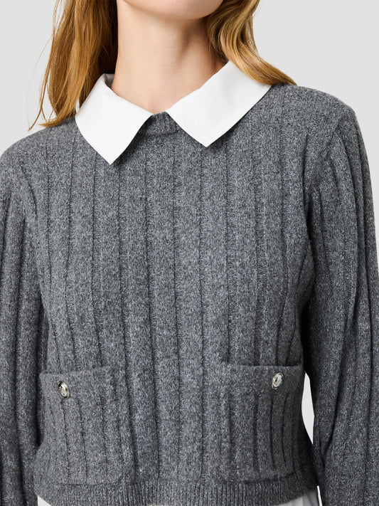 A close-up of a woman wearing a gray ribbed knit sweater with a contrasting white pointed collar. The sweater features vertical ribbing, long sleeves, and two front patch pockets with decorative silver-tone buttons.