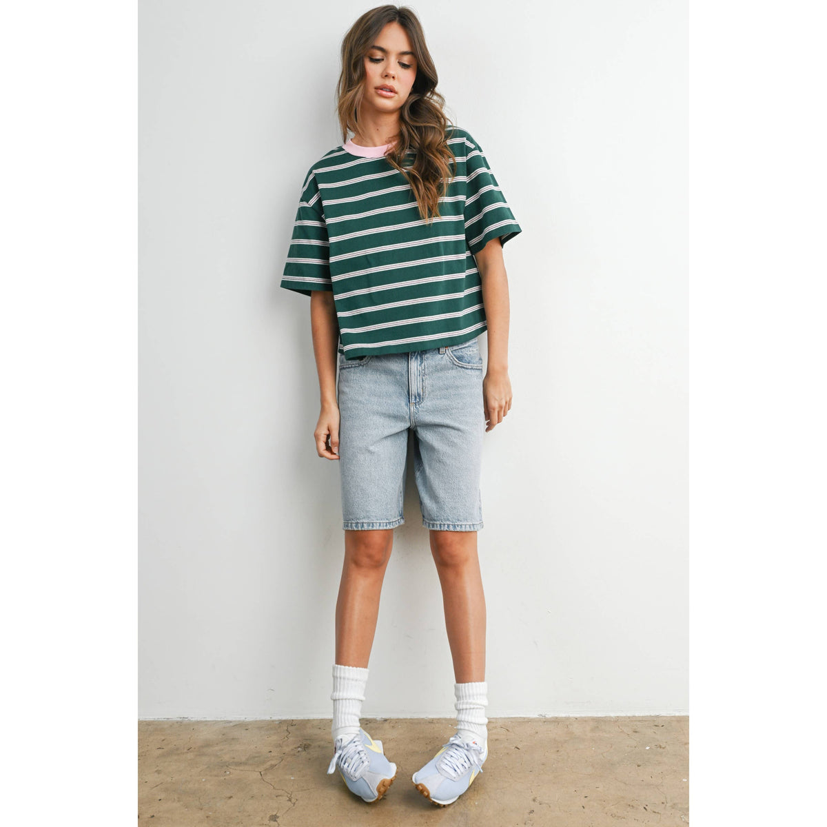 Woman wearing a green and white striped shirt with denim shorts against a plain background