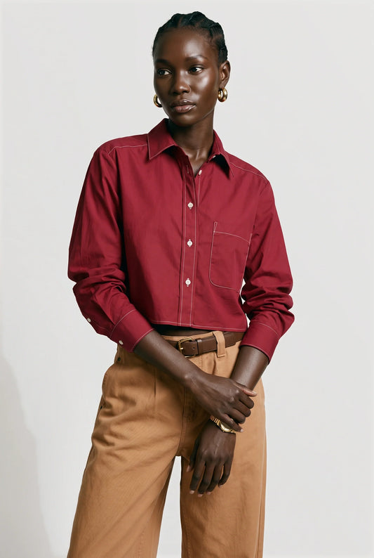 A model wearing a long-sleeve burgundy button-down shirt tucked into tan trousers, standing against a light gray studio background.