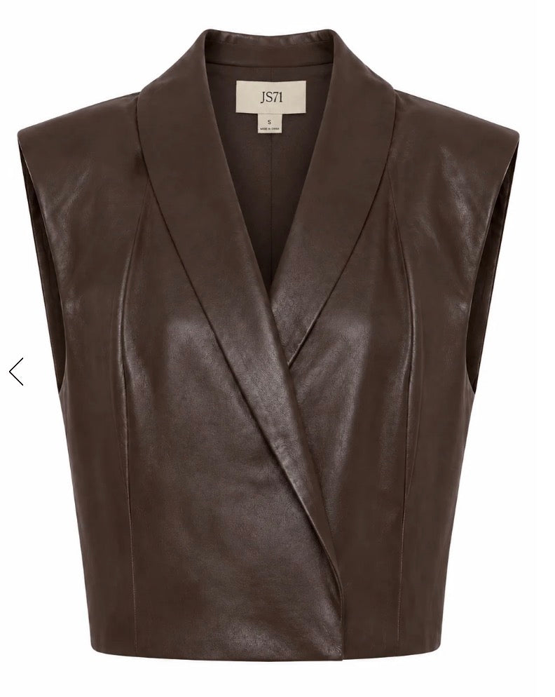A sleeveless dark brown faux-leather vest with a shawl collar and wrap-style front, shown on a plain white background. The brand label inside the collar reads 'JST'.