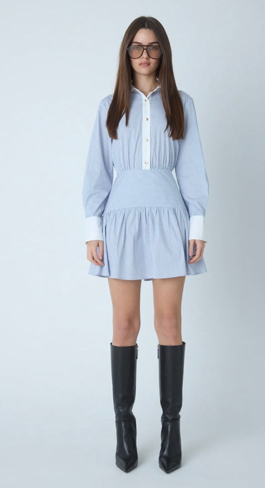 A woman modeling a light blue long-sleeve mini dress with white trim and buttons, paired with black knee-high boots, against a light gray studio background.