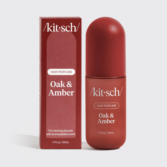 A bottle of Kit Sch Hair Perfume Oak & Amber next to its matching box packaging, both in a deep reddish-brown color, on a light gray background.
