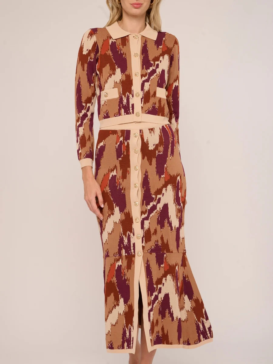 A woman modeling a long-sleeve midi dress with a beige, brown, and burgundy ikat pattern, featuring a pointed collar, button front, and matching waist tie.