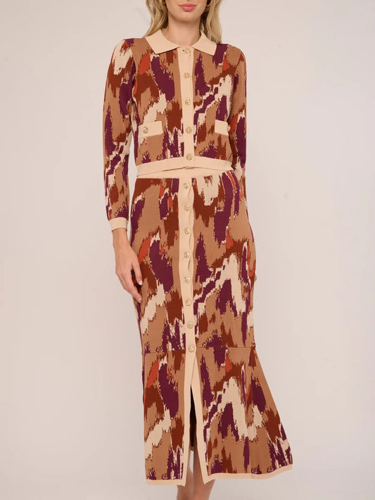 A woman modeling a long-sleeve midi dress with a beige, brown, and burgundy ikat pattern, featuring a pointed collar, button front, and matching waist tie.