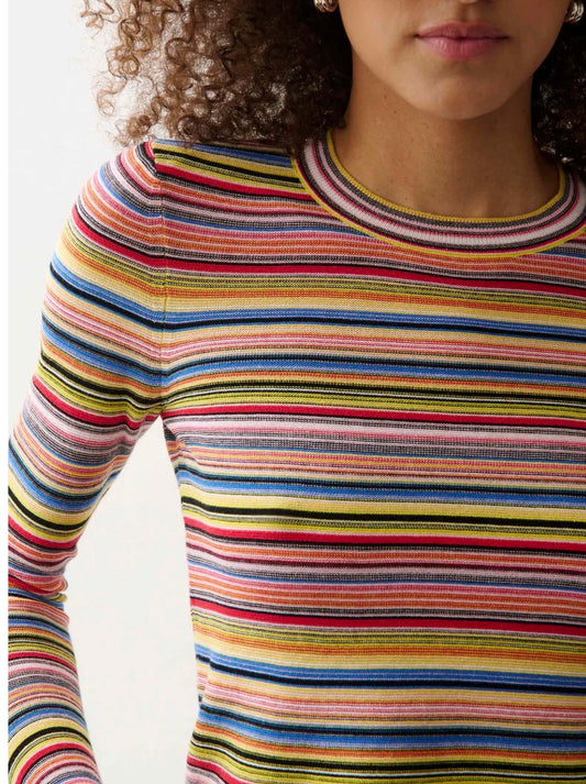A close-up of a model wearing a long-sleeve crewneck knit top with horizontal multicolor stripes including yellow, blue, red, pink, green, and black on a white background.