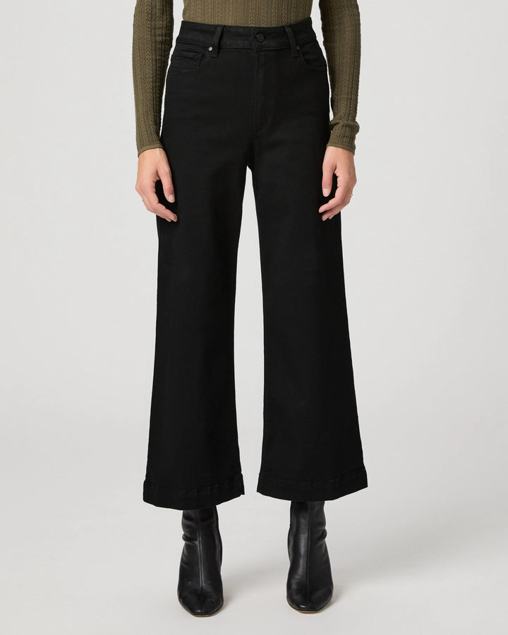 A model is shown from the waist down wearing black wide-leg cropped jeans, a textured olive green long-sleeve top, and black leather ankle boots, set against a plain light gray studio background.