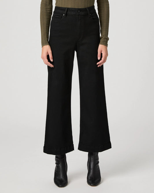 A model is shown from the waist down wearing black wide-leg cropped jeans, a textured olive green long-sleeve top, and black leather ankle boots, set against a plain light gray studio background.