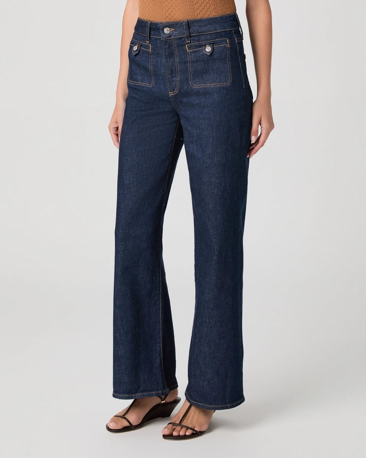A model wearing dark blue high-waisted wide-leg jeans with a straight-to-flared leg, paired with brown wedge sandals against a light gray studio background.