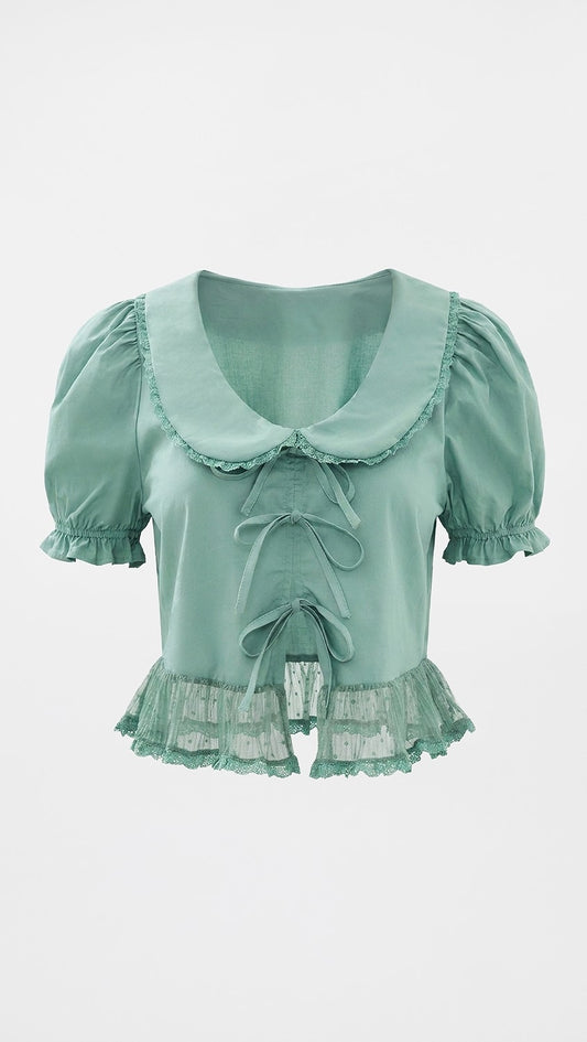 A mint green short-sleeve blouse with a large ruffled Peter Pan collar, front tie details, and a ruffled lace hem, shown against a plain light gray background.