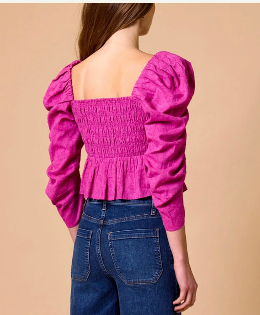 Person wearing a pink blouse with long sleeves and blue jeans on a beige background