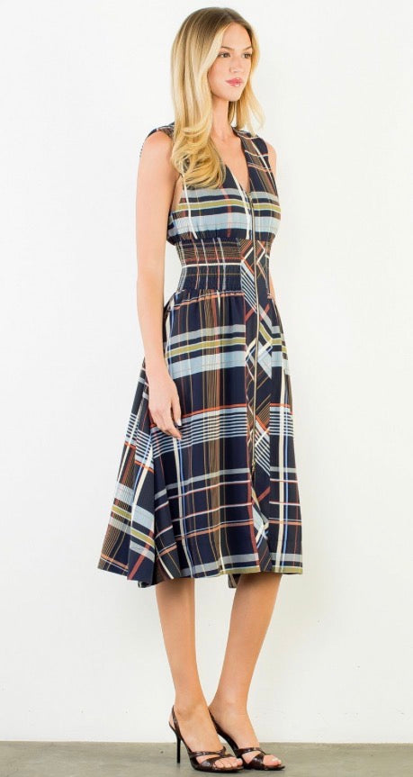 A woman modeling a sleeveless midi dress with a navy blue and black plaid pattern accented with thin yellow, orange, and white stripes. She is wearing black strappy high-heeled sandals against a plain white studio background.