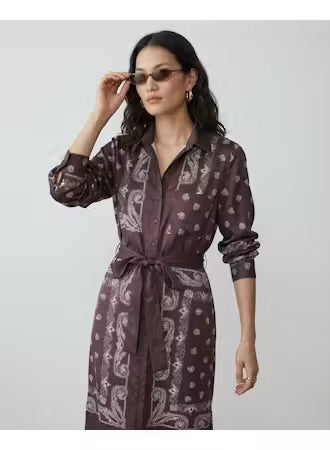 A woman modeling a long-sleeve, button-front shirt dress with a matching waist tie. The dress has a dark brown base with a white paisley and polka dot pattern.
