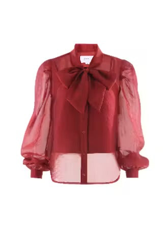 A sheer red long-sleeve blouse with a large bow at the collar, a button front, and a sheer underlayer visible at the hem and sleeves, shown on a plain white background.
