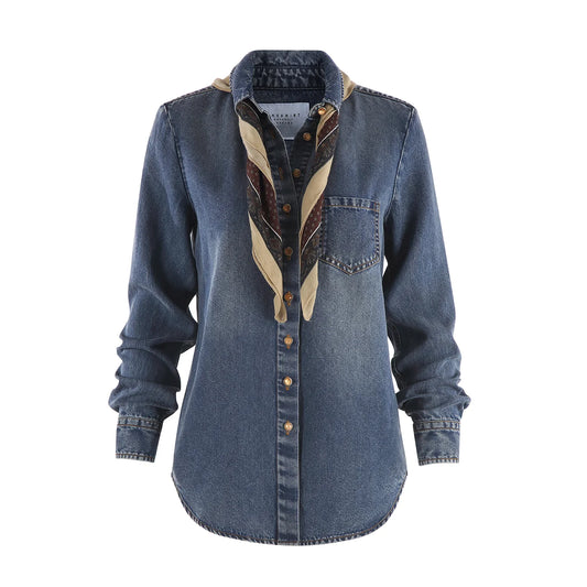 A women's long-sleeve button-up shirt in medium blue denim, featuring a decorative beige and brown patterned scarf draped over the collar and down the front placket, with brown buttons. The shirt has a chest pocket and is shown against a plain white background.