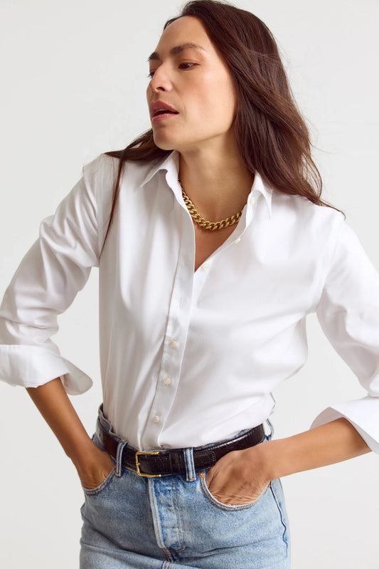 Woman wearing a white shirt and blue jeans with a gold necklace on a plain background